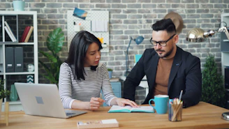 a man and a woman sitting at a table looking at a laptop