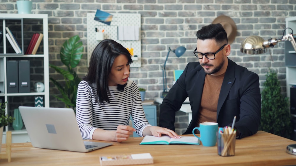 a man and a woman sitting at a table looking at a laptop