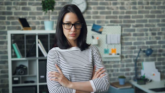 a woman wearing glasses standing in front of a brick wall
