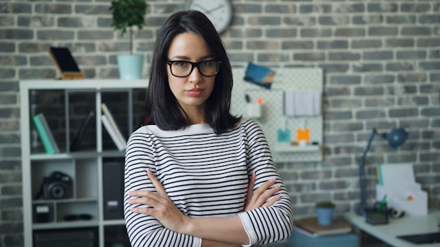 a woman wearing glasses standing in front of a brick wall
