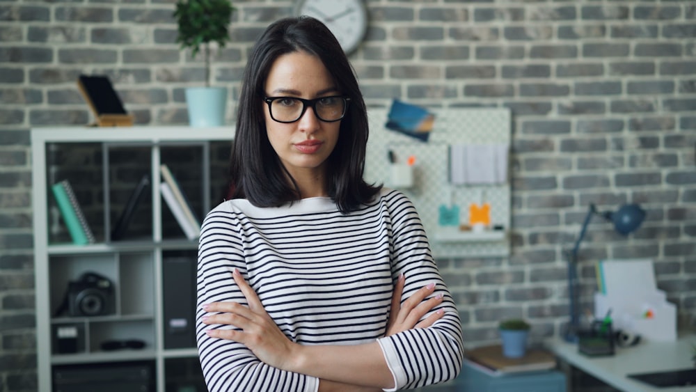 a woman wearing glasses standing in front of a brick wall