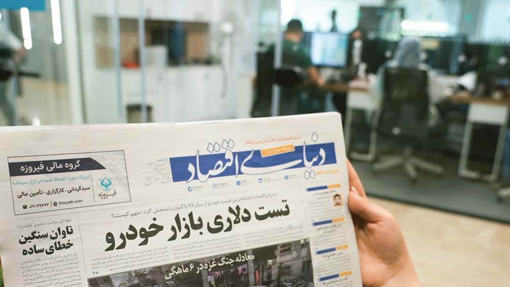 a person holding up a newspaper with arabic writing