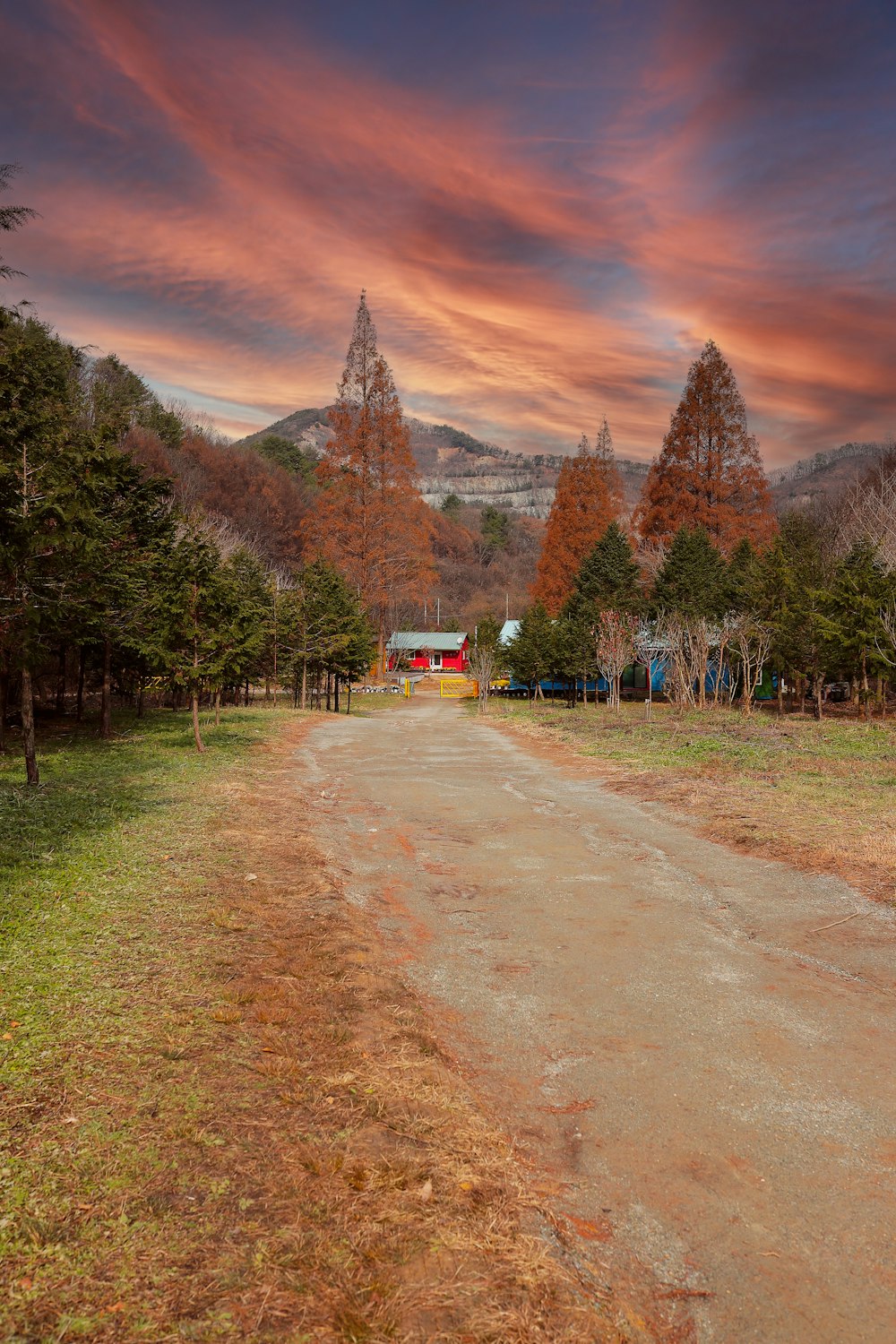 a dirt road with a red barn in the distance