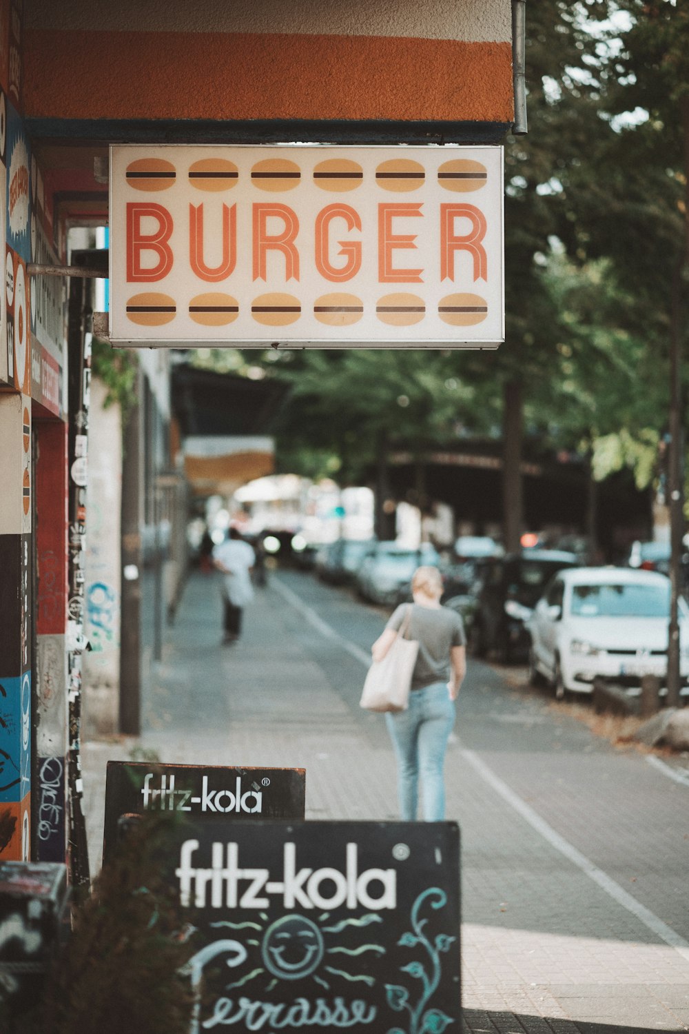 a woman walking down a street past a burger restaurant
