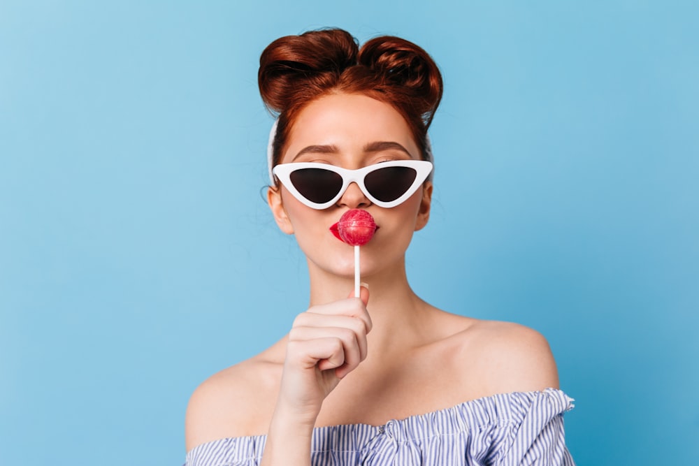 a woman wearing sunglasses and holding a lollipop