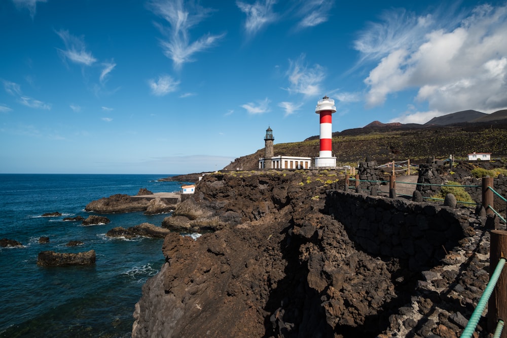 a red and white light house sitting on top of a cliff next to the ocean