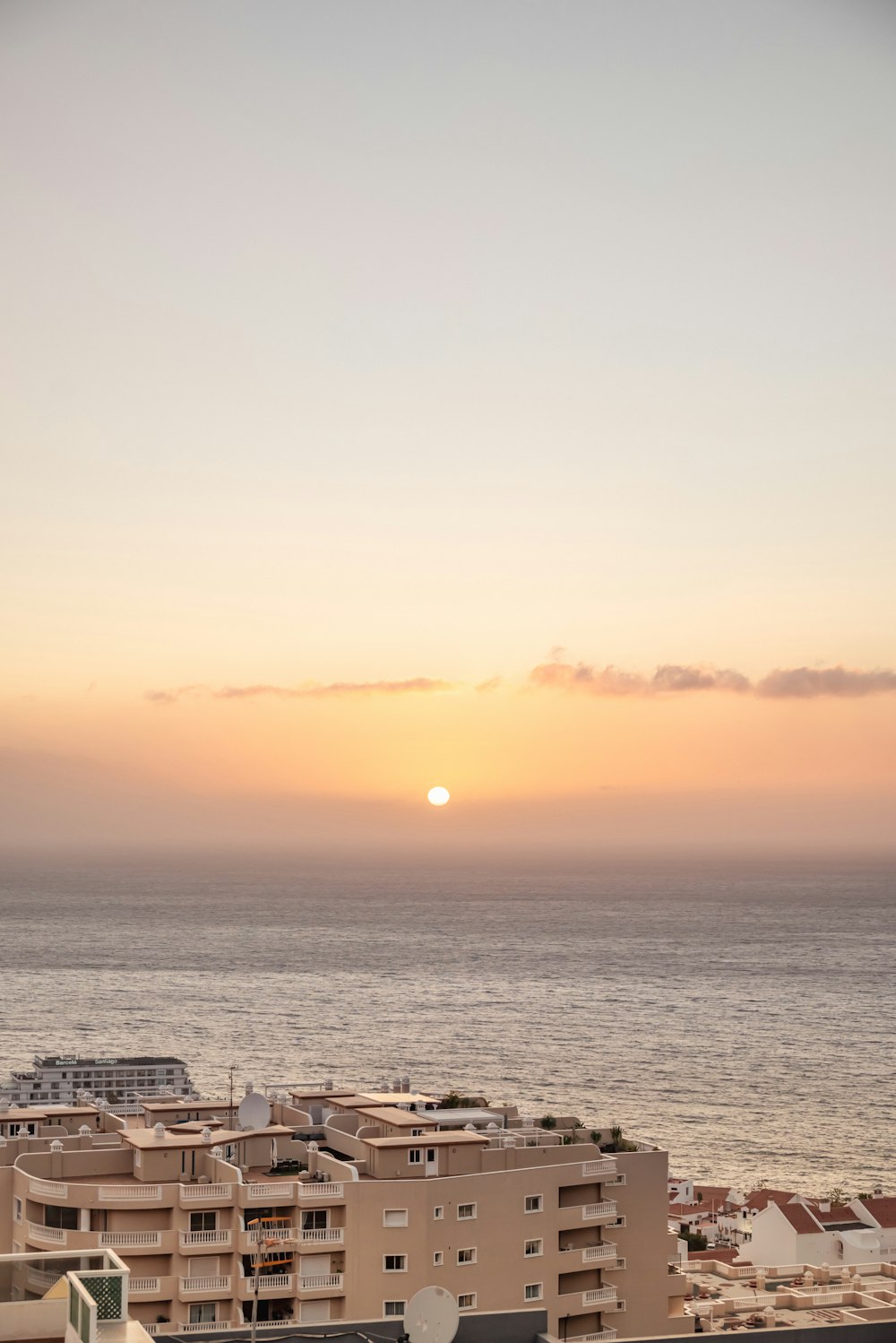 the sun is setting over a city by the ocean