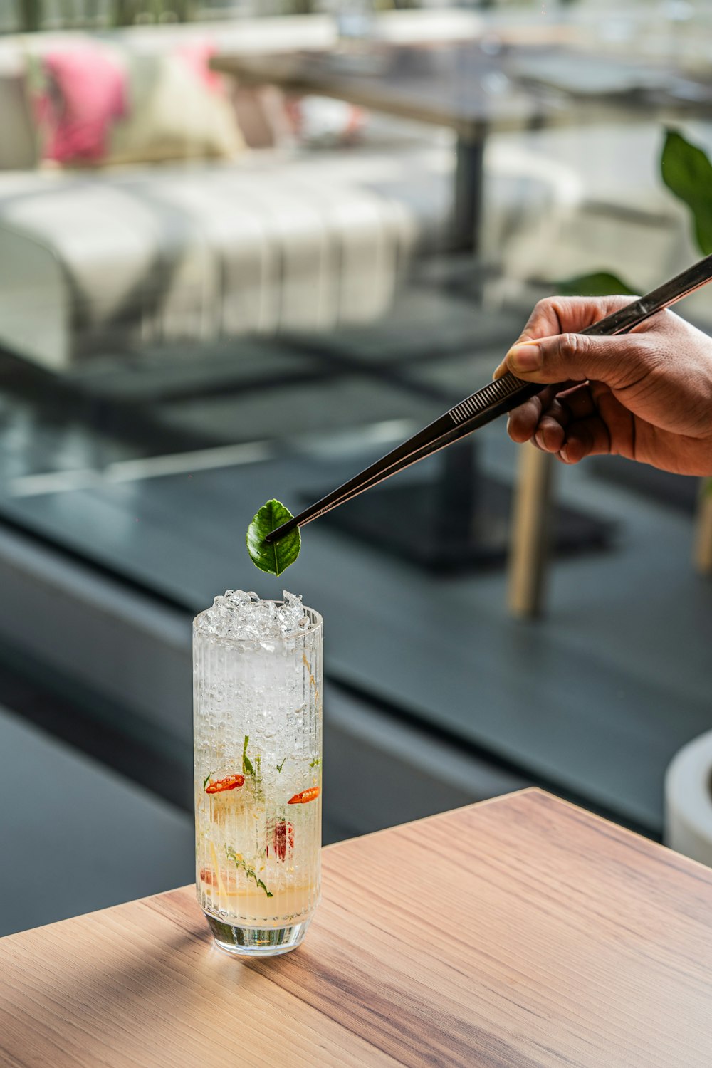 a person holding chopsticks above a tall glass filled with liquid