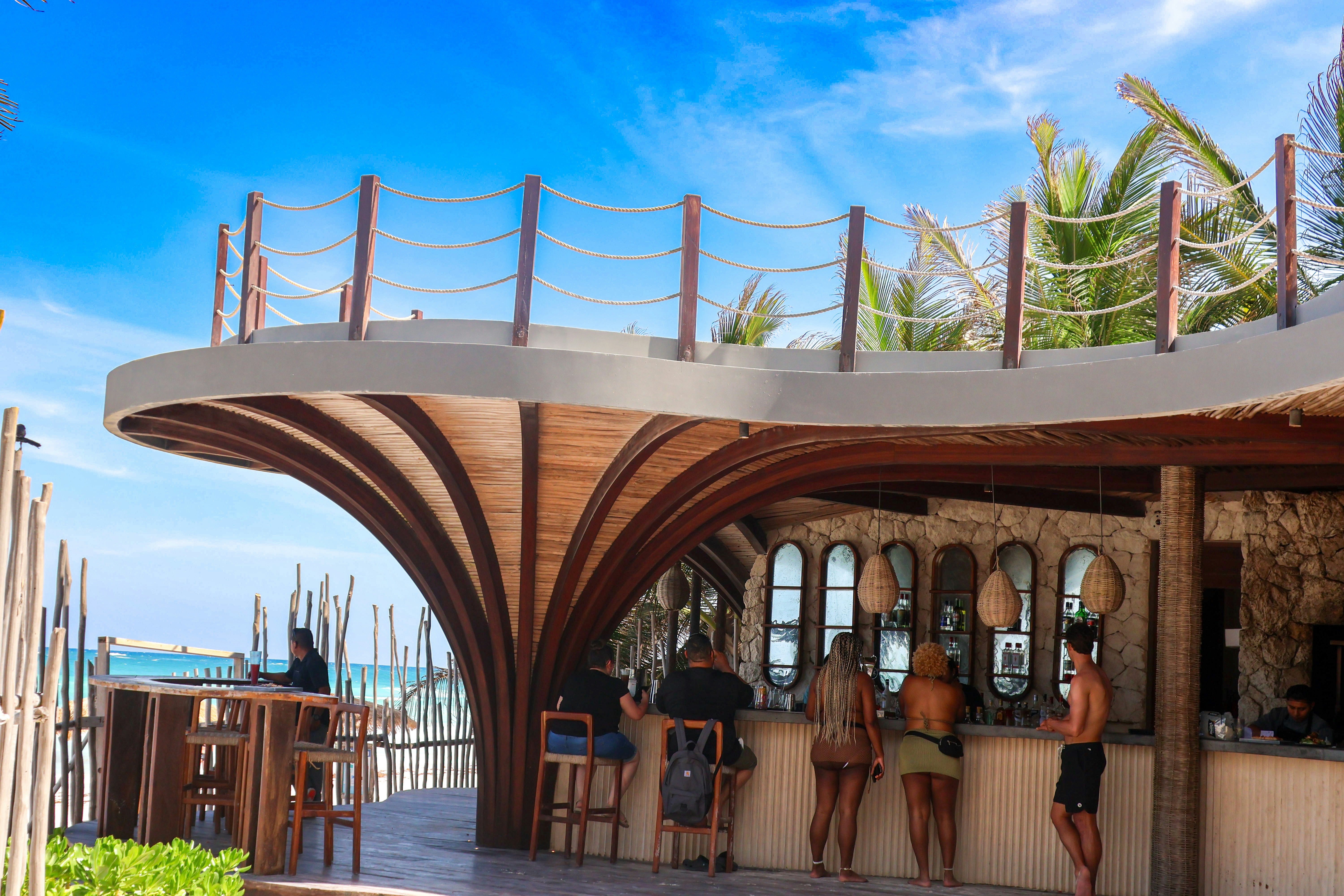 a group of people sitting at a bar next to the ocean, Beach in Tulum