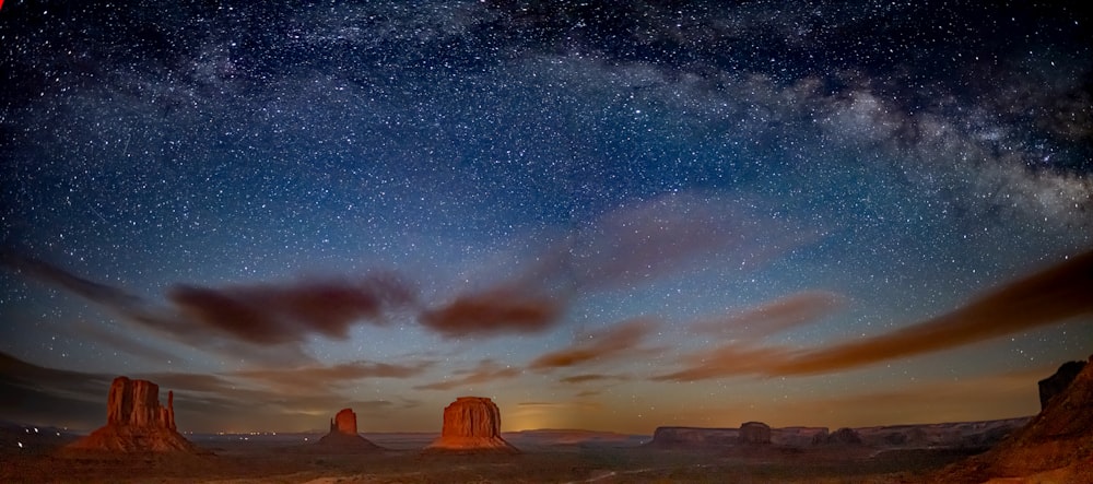the night sky with stars and clouds above a desert landscape