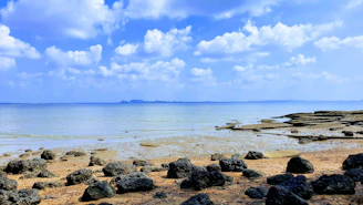 a beach with rocks and water under a cloudy blue sky