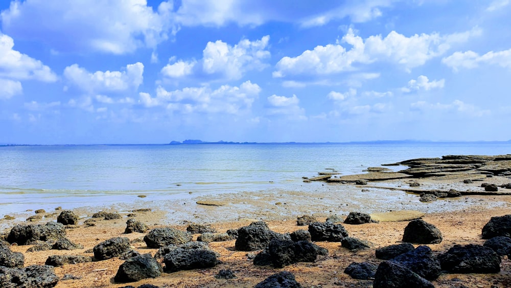 a beach with rocks and water under a cloudy blue sky