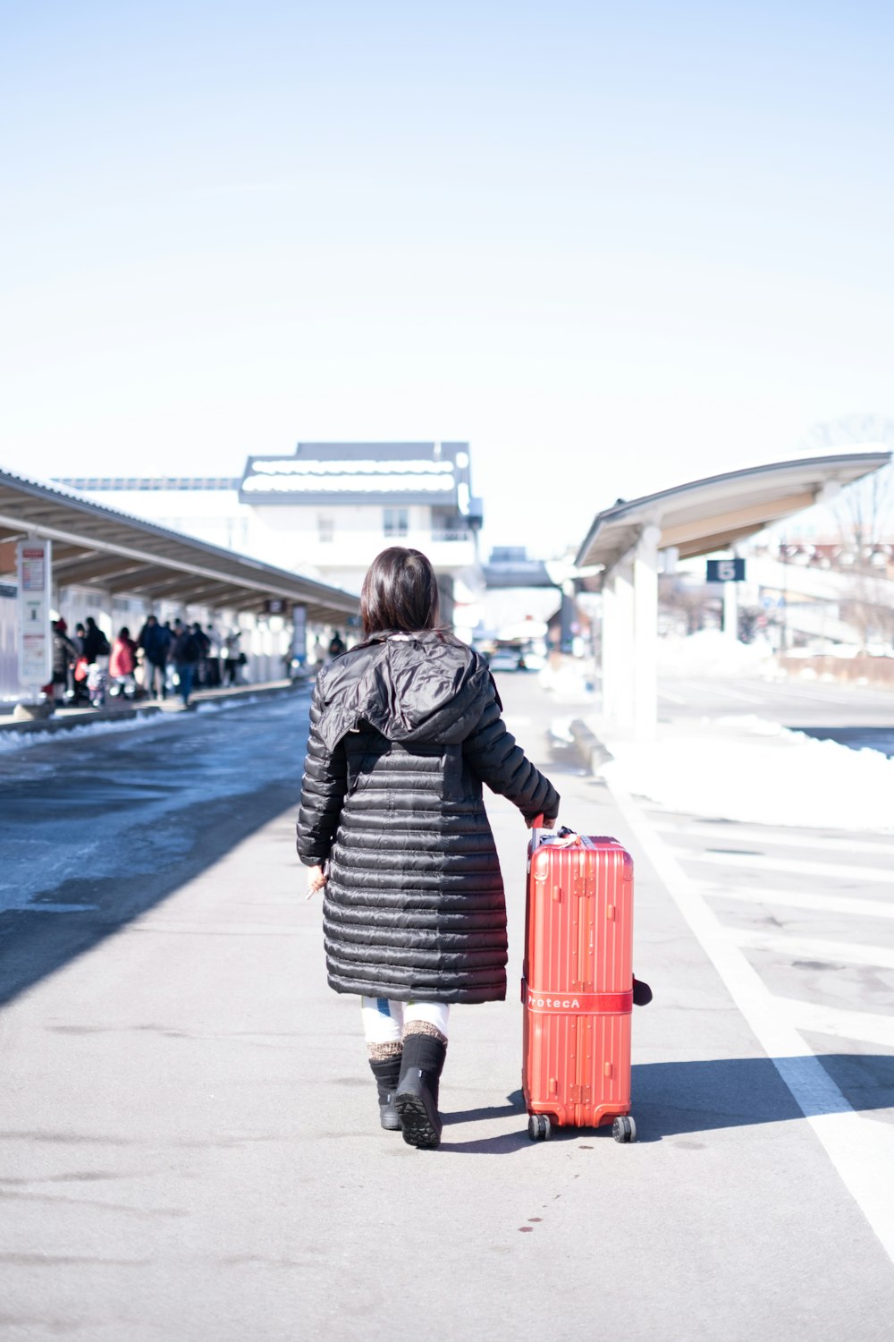 a woman walking down a sidewalk with a red suitcase