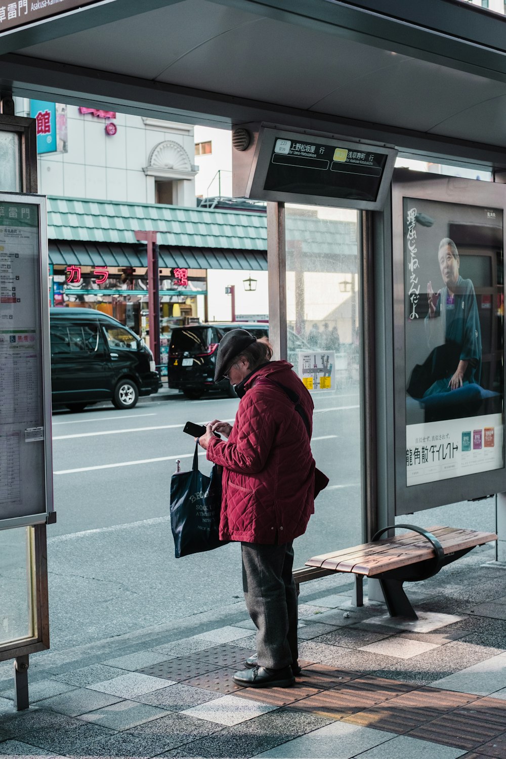 a man in a red jacket standing at a bus stop