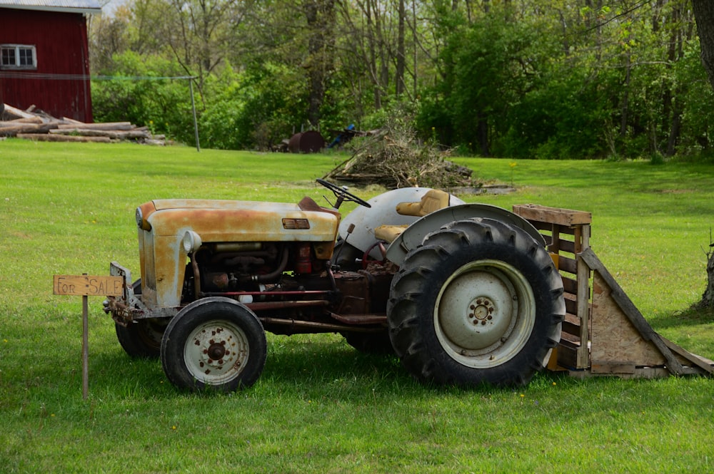 an old tractor sitting in the grass next to a tree