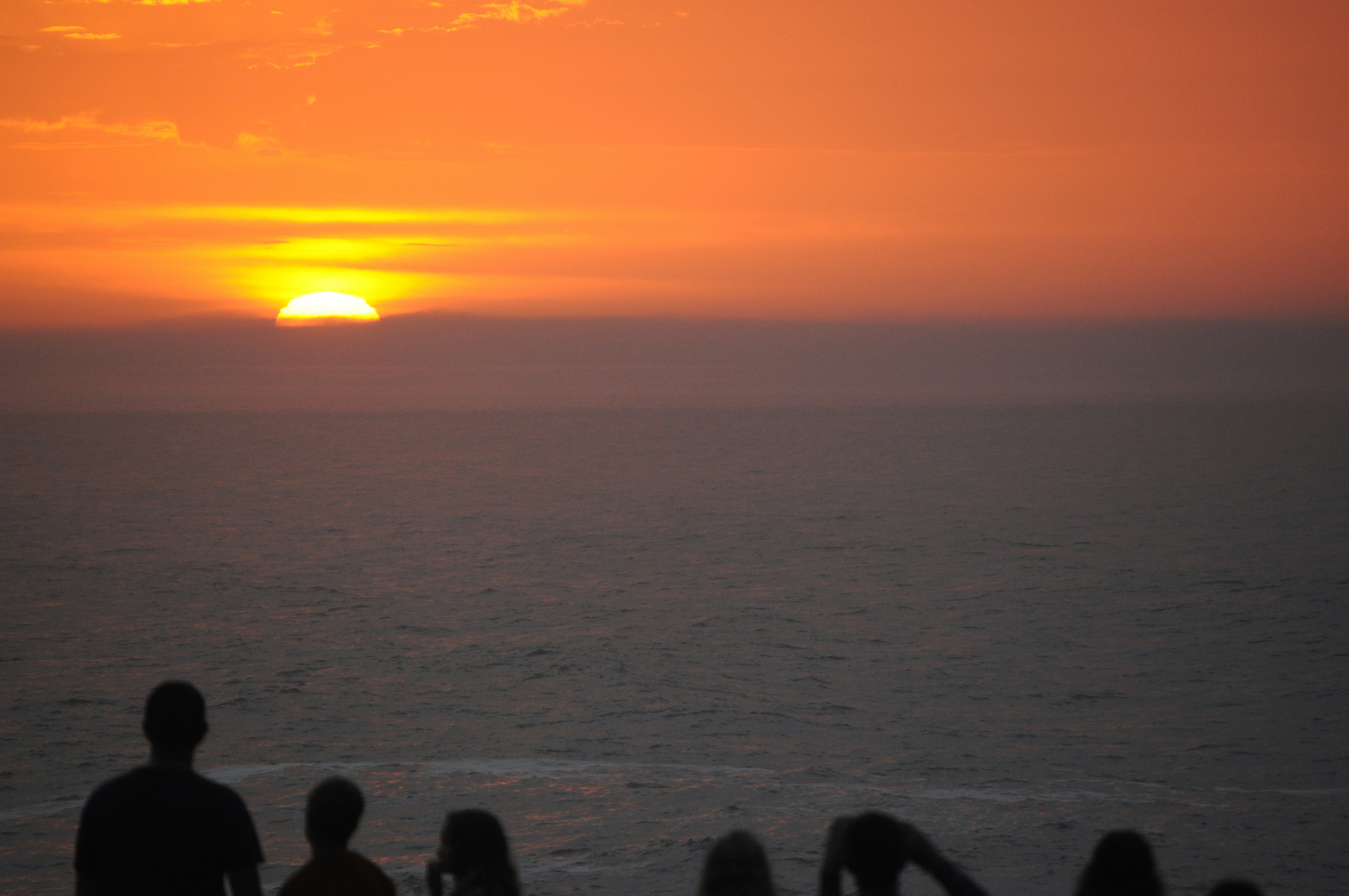 a group of people watching the sun set over the ocean