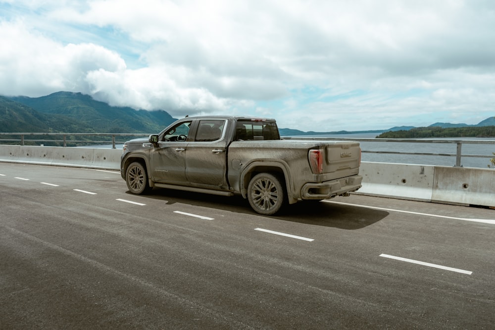 a silver truck driving down a highway next to a body of water