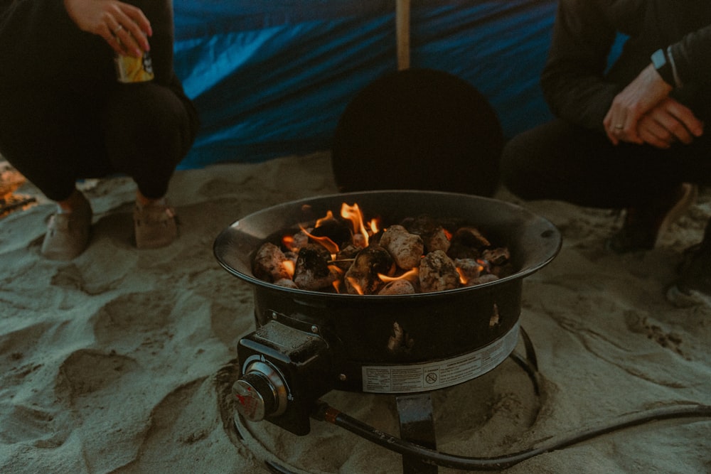 two people sitting in the sand next to a campfire