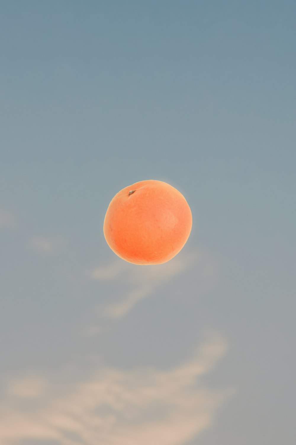 an orange flying through the air with a sky background