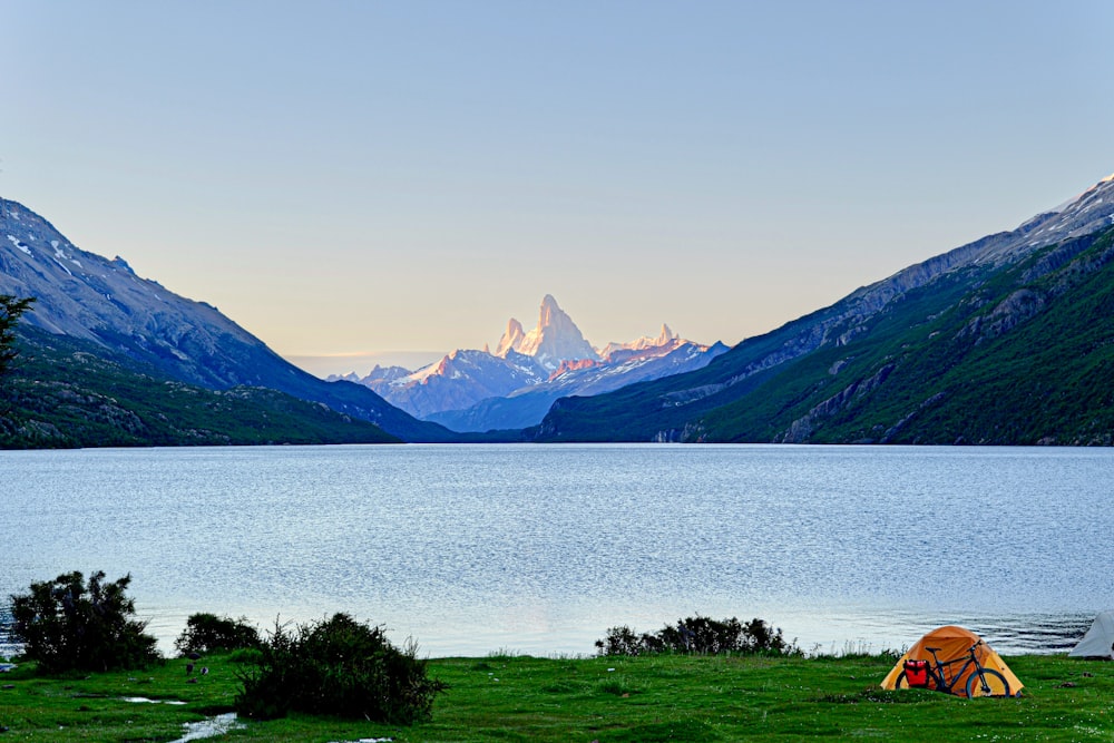 a tent is set up on the shore of a lake with mountains in the background