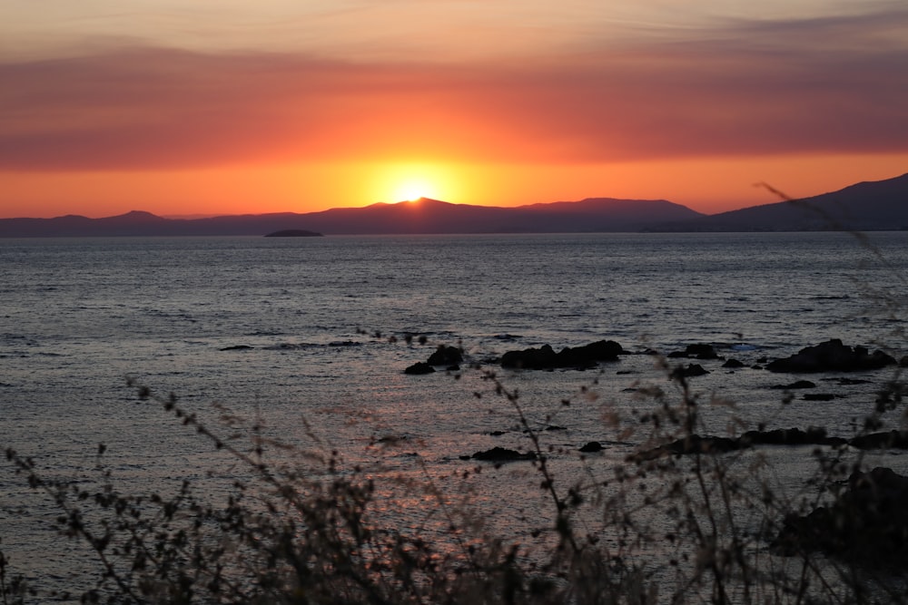 a sunset over a body of water with mountains in the background