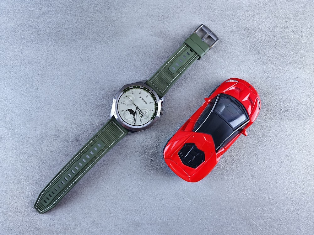 a red toy car next to a green watch
