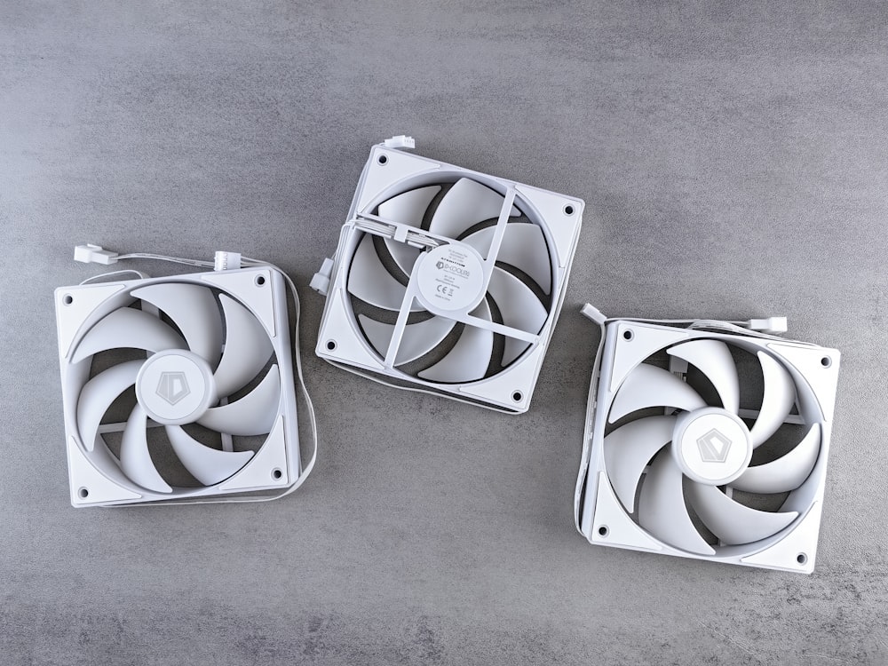 three white fans sitting on top of a cement floor