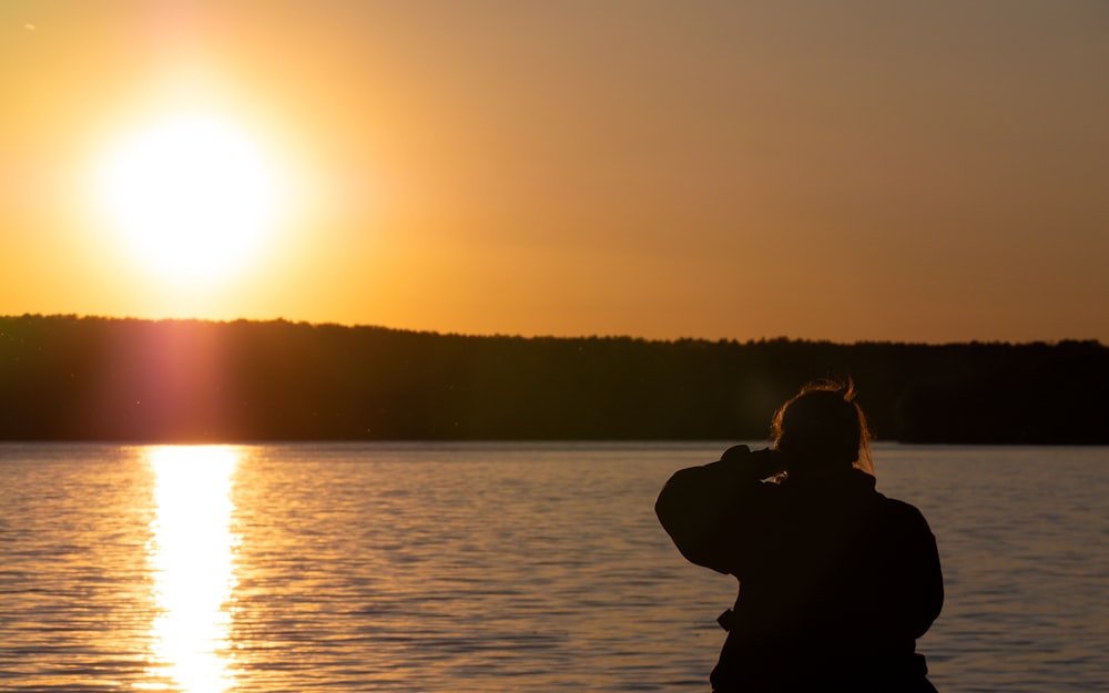 a person taking a picture of the sun setting over a lake