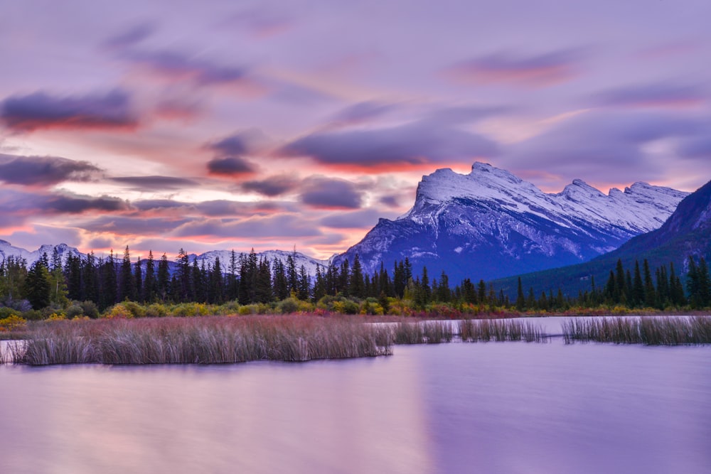 a lake surrounded by trees and mountains under a cloudy sky