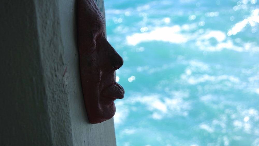 a close up of a face on a wall near a body of water