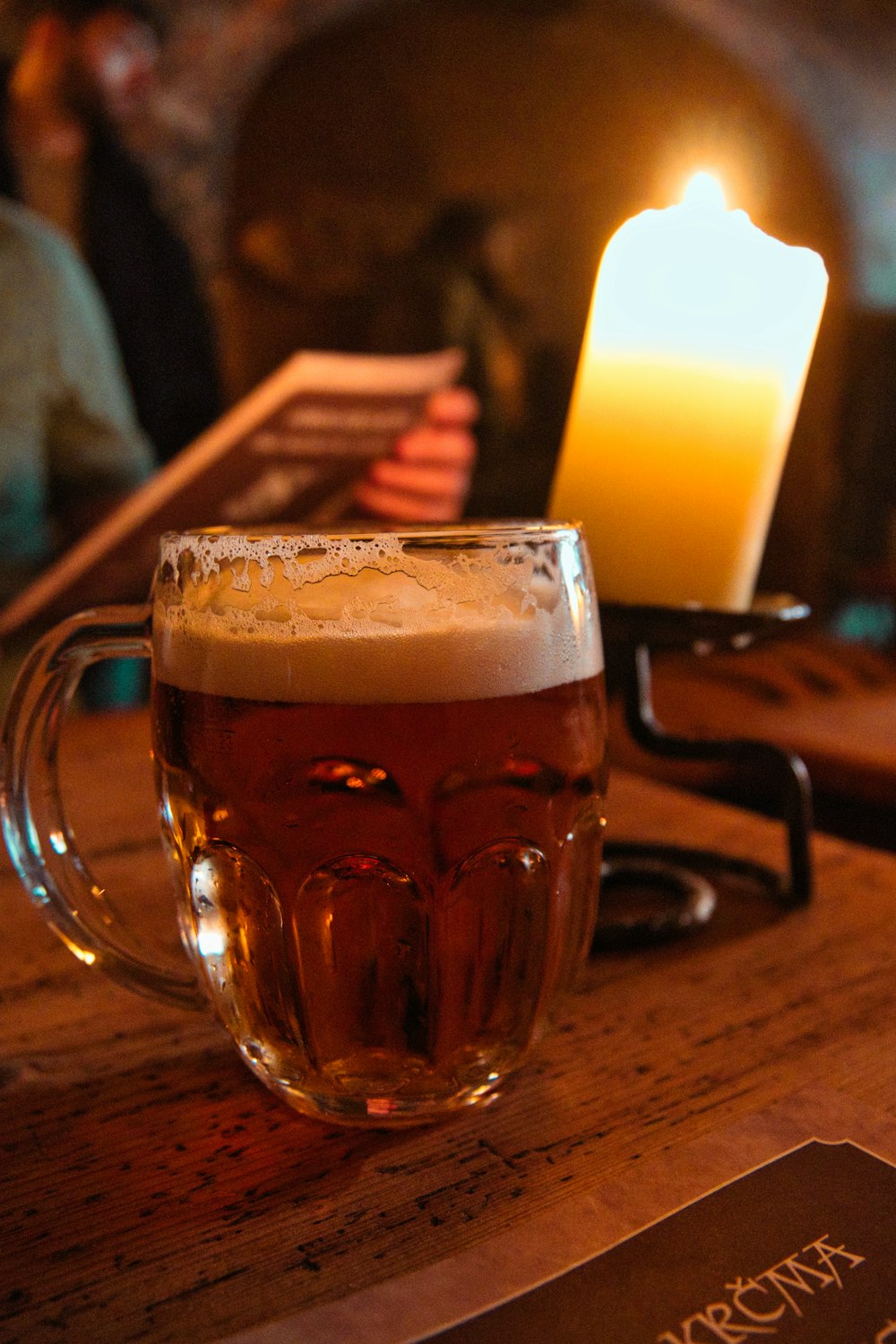 a glass of beer sitting on a table next to a candle