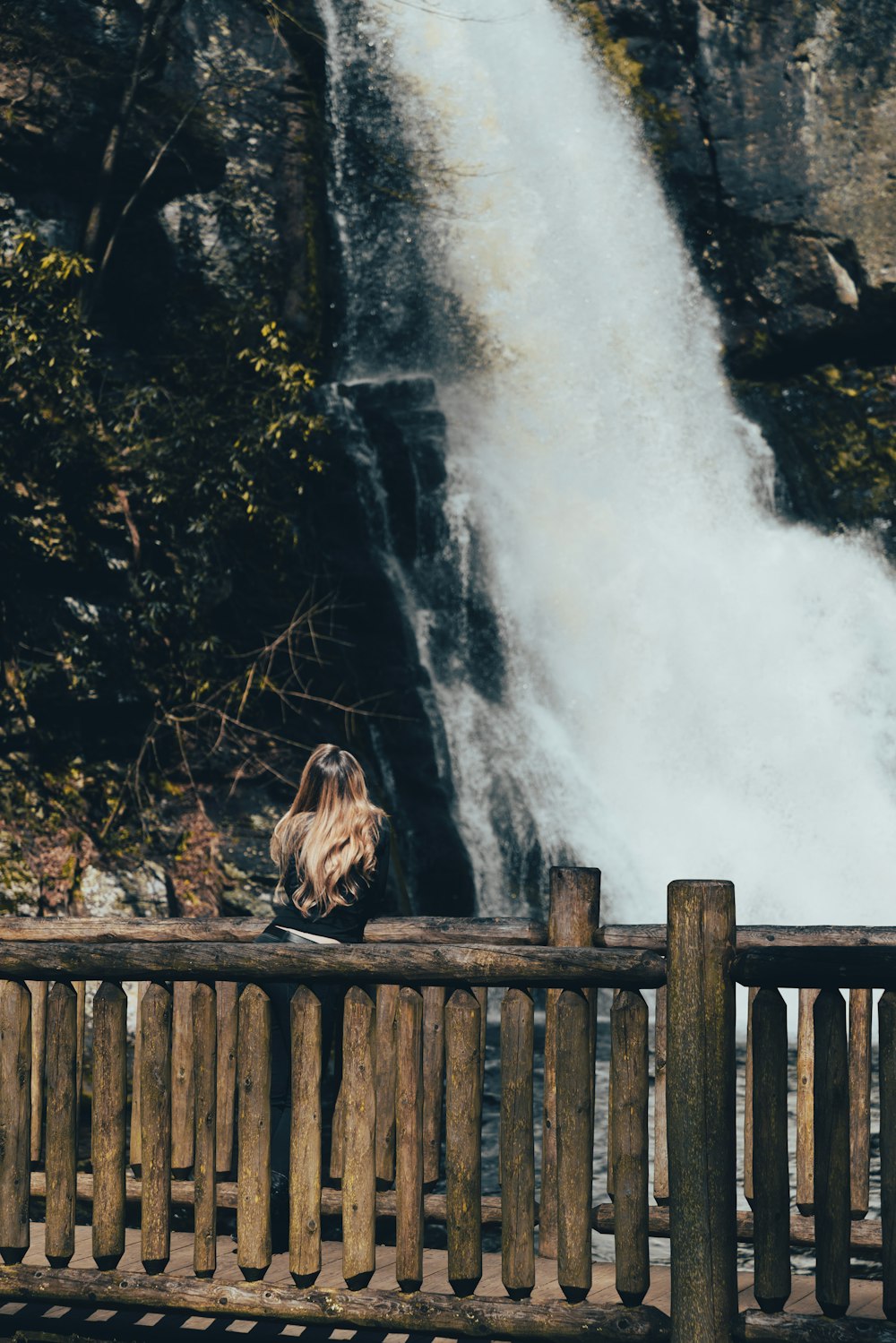 a woman sitting on a wooden bench next to a waterfall