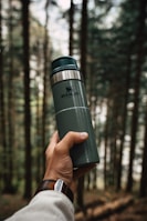 a hand holding a green travel mug in a forest