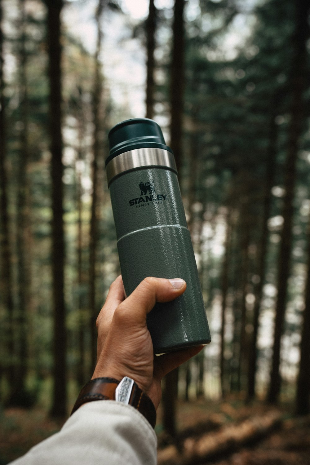 a hand holding a green travel mug in a forest