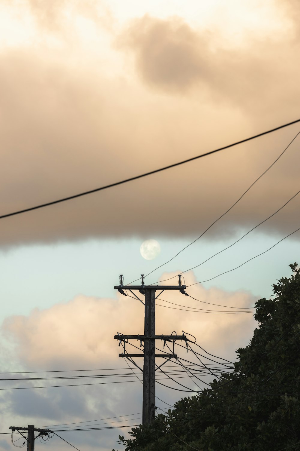 a full moon is seen through the clouds above power lines