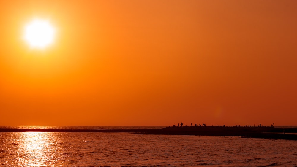 the sun is setting over the ocean with a boat in the water