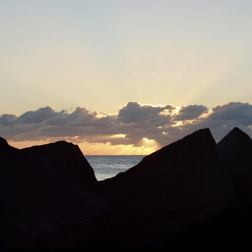 the sun is setting over the ocean with rocks in the foreground