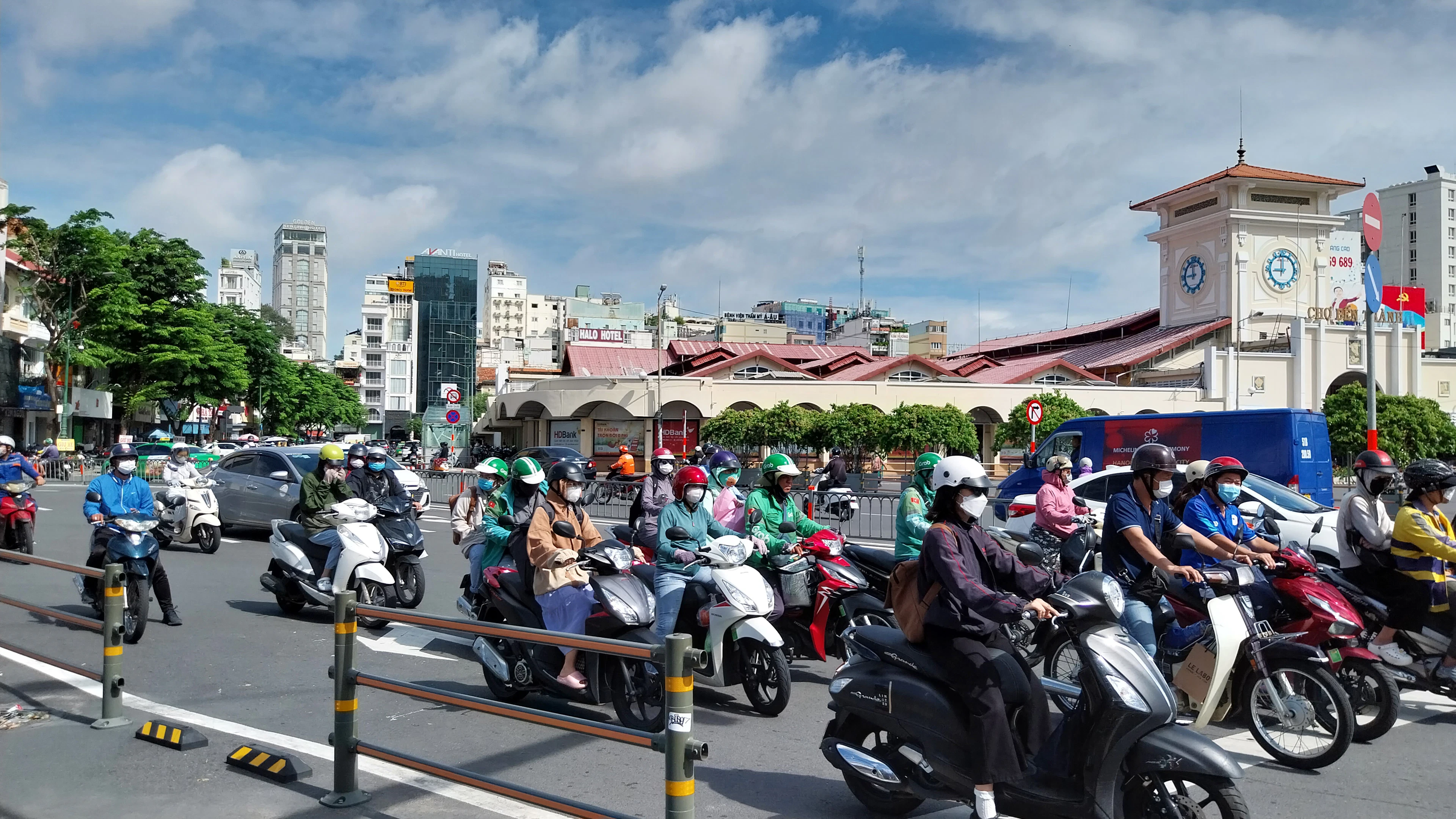 Ben Thanh Market's clock tower overlooking a street thick with motorbikes under a blue sky.