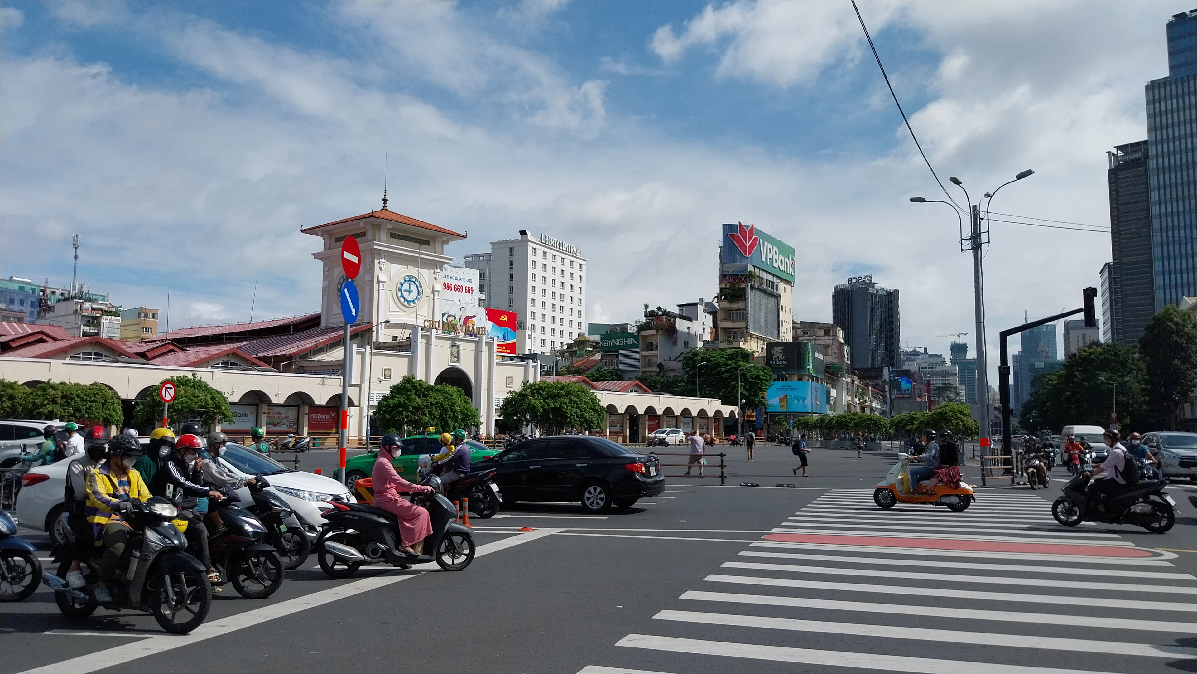 Ben Thanh Market's clock tower and colonial facade above a busy intersection full of motorbikes.