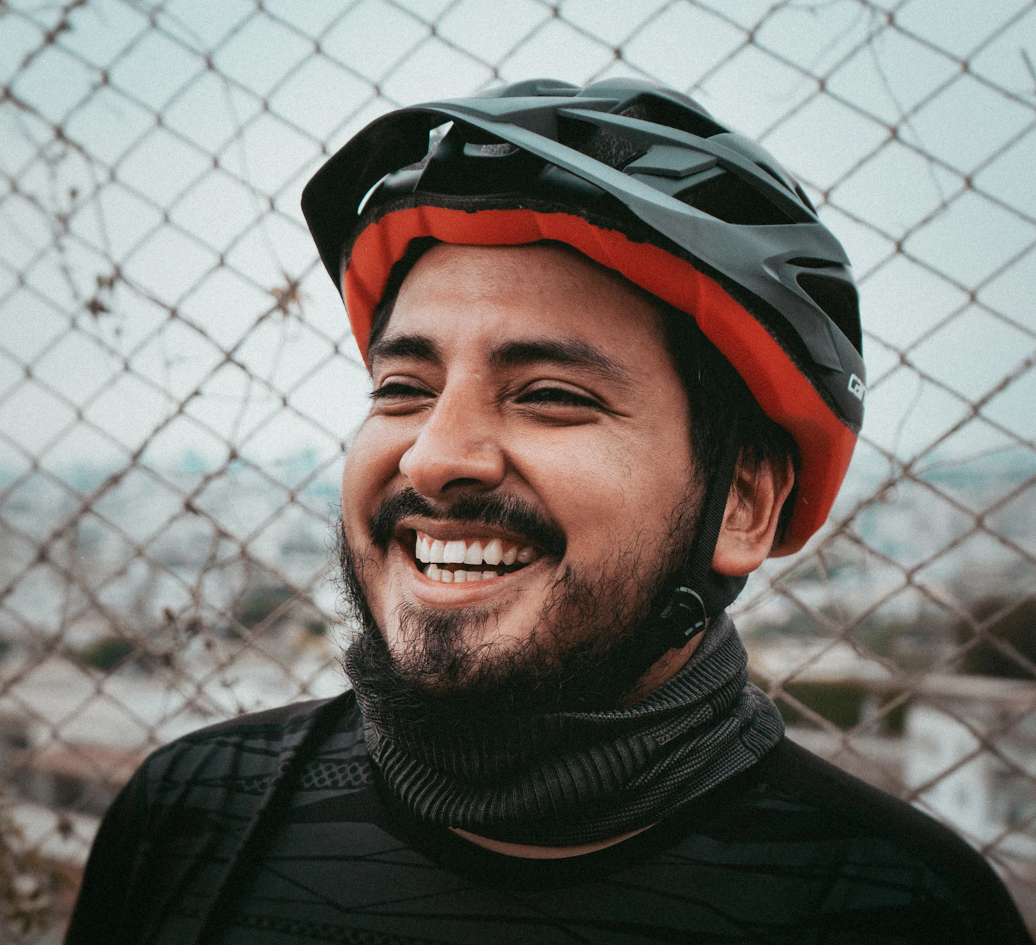 A smiling cyclist in a red helmet beside a wire fence