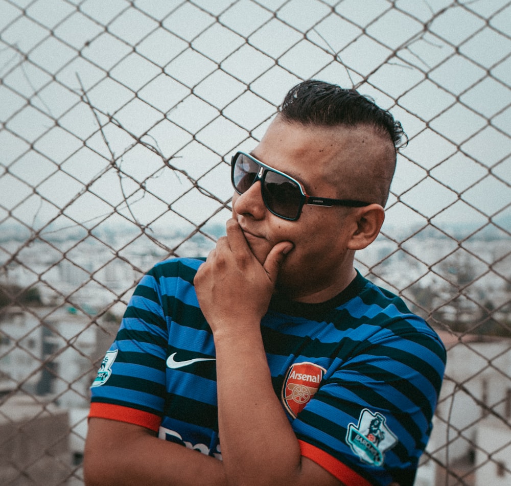 a man wearing sunglasses leaning against a fence