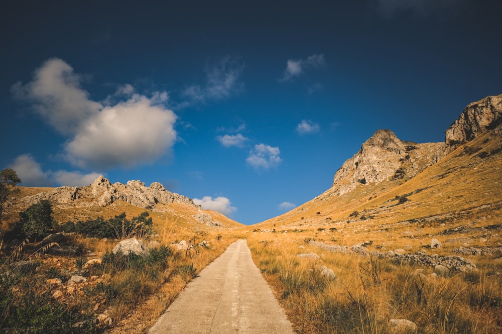 a dirt road surrounded by mountains under a blue sky