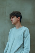 a young man in a blue sweater leaning against a wall