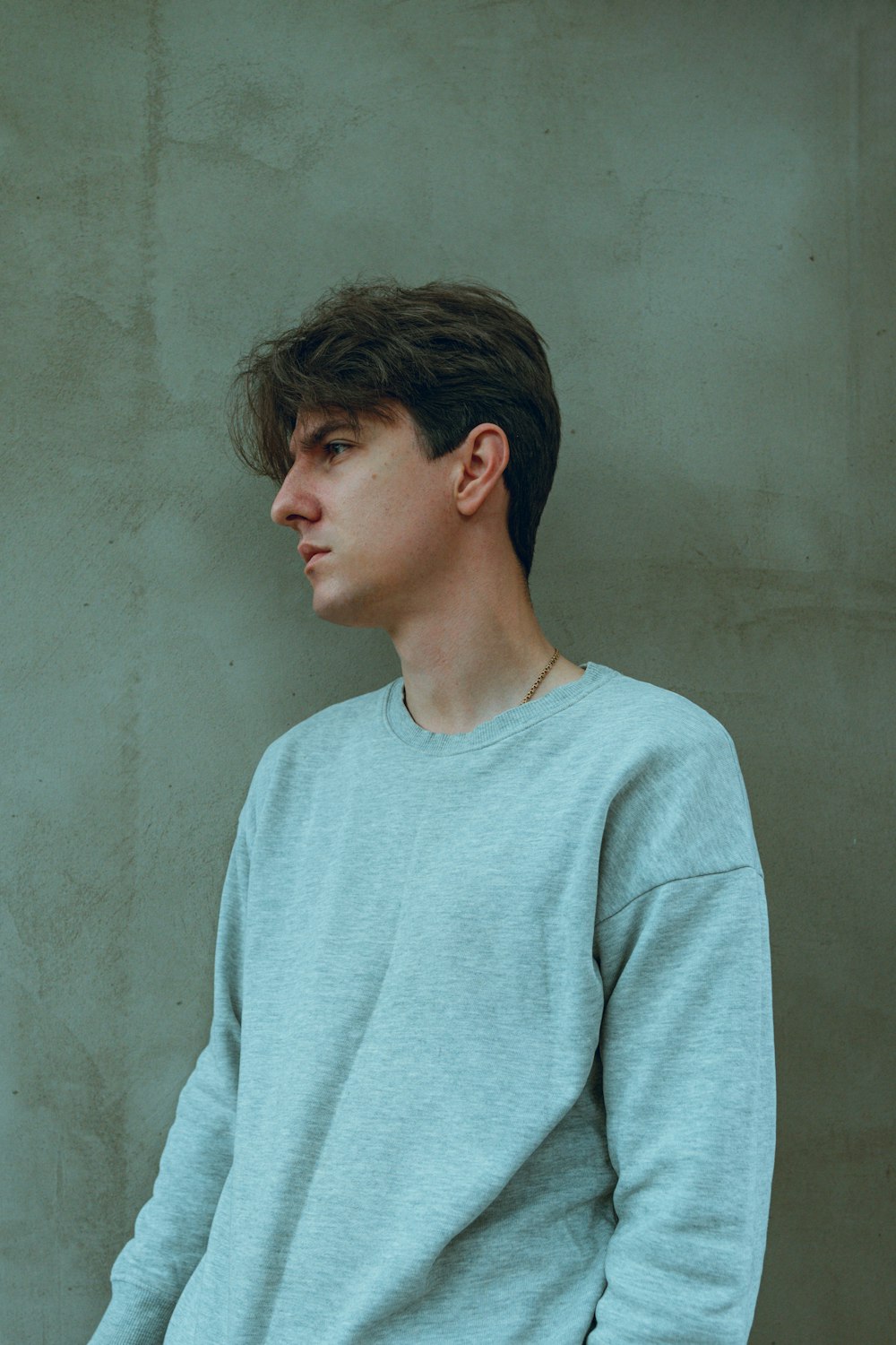 a young man in a blue sweater leaning against a wall