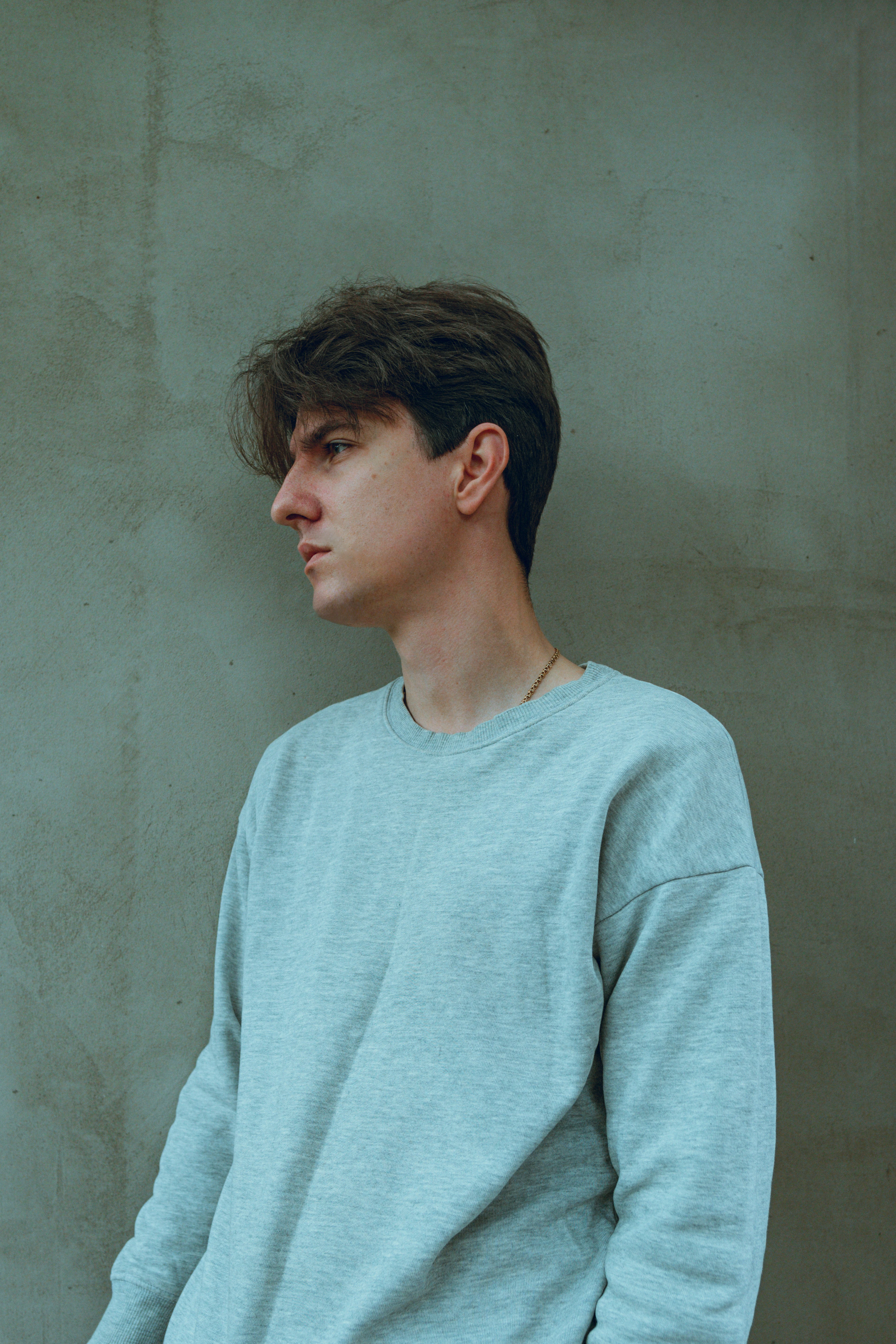 Young man in a mint crewneck sweatshirt against a green wall