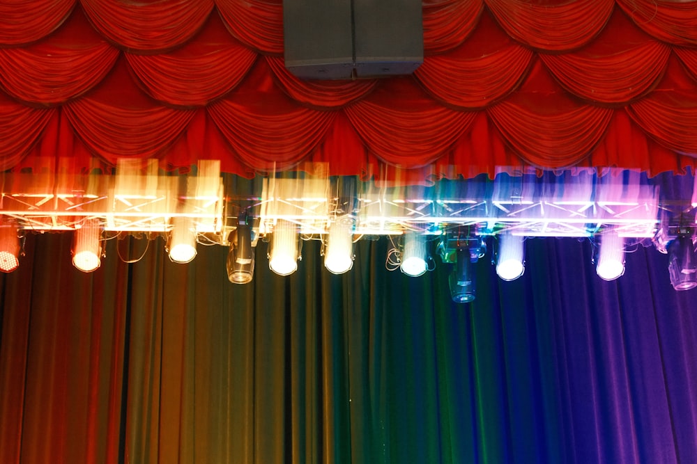 a row of lights hanging from a ceiling in front of a rainbow colored curtain