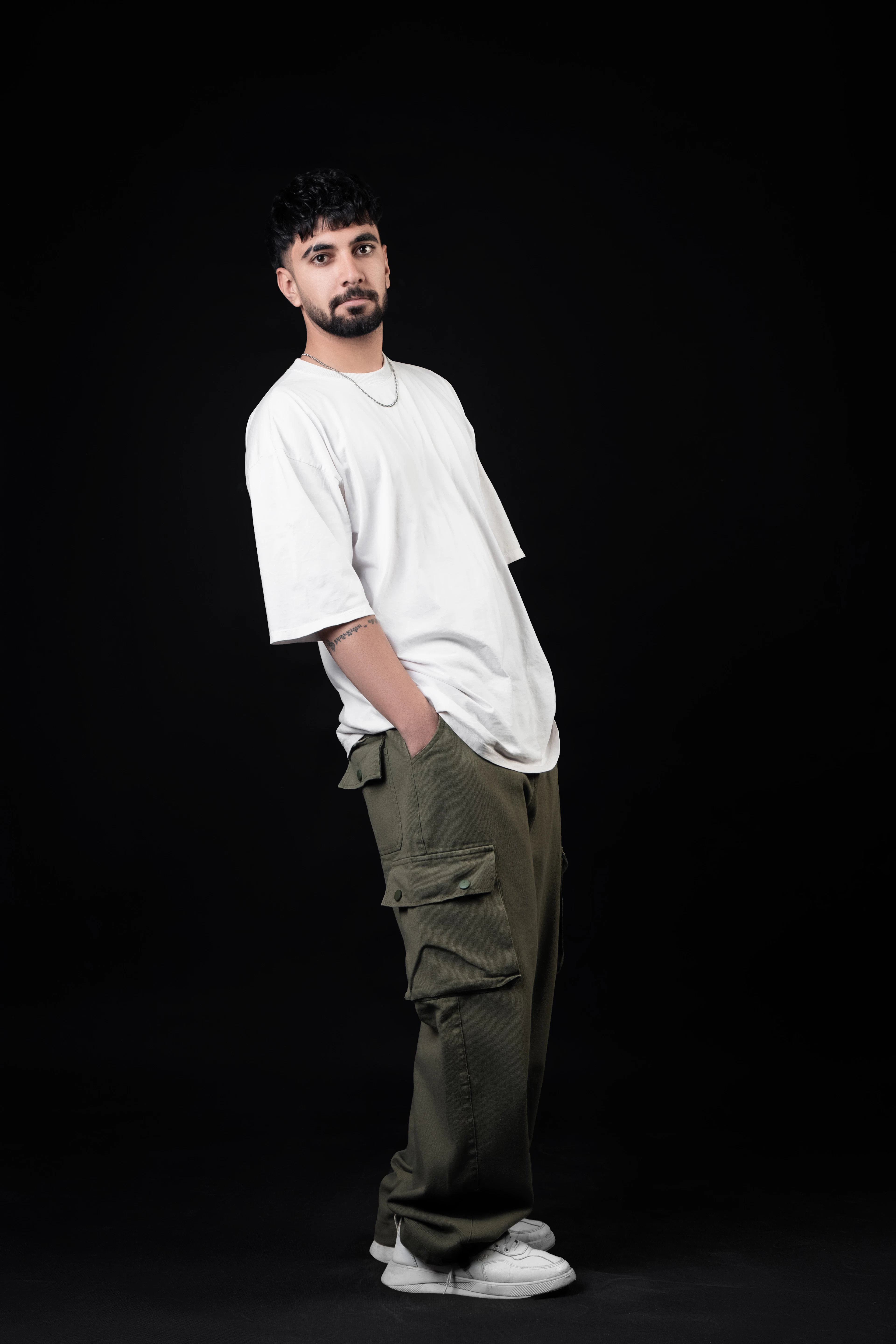 Man in a white tee and olive cargo pants against a black backdrop