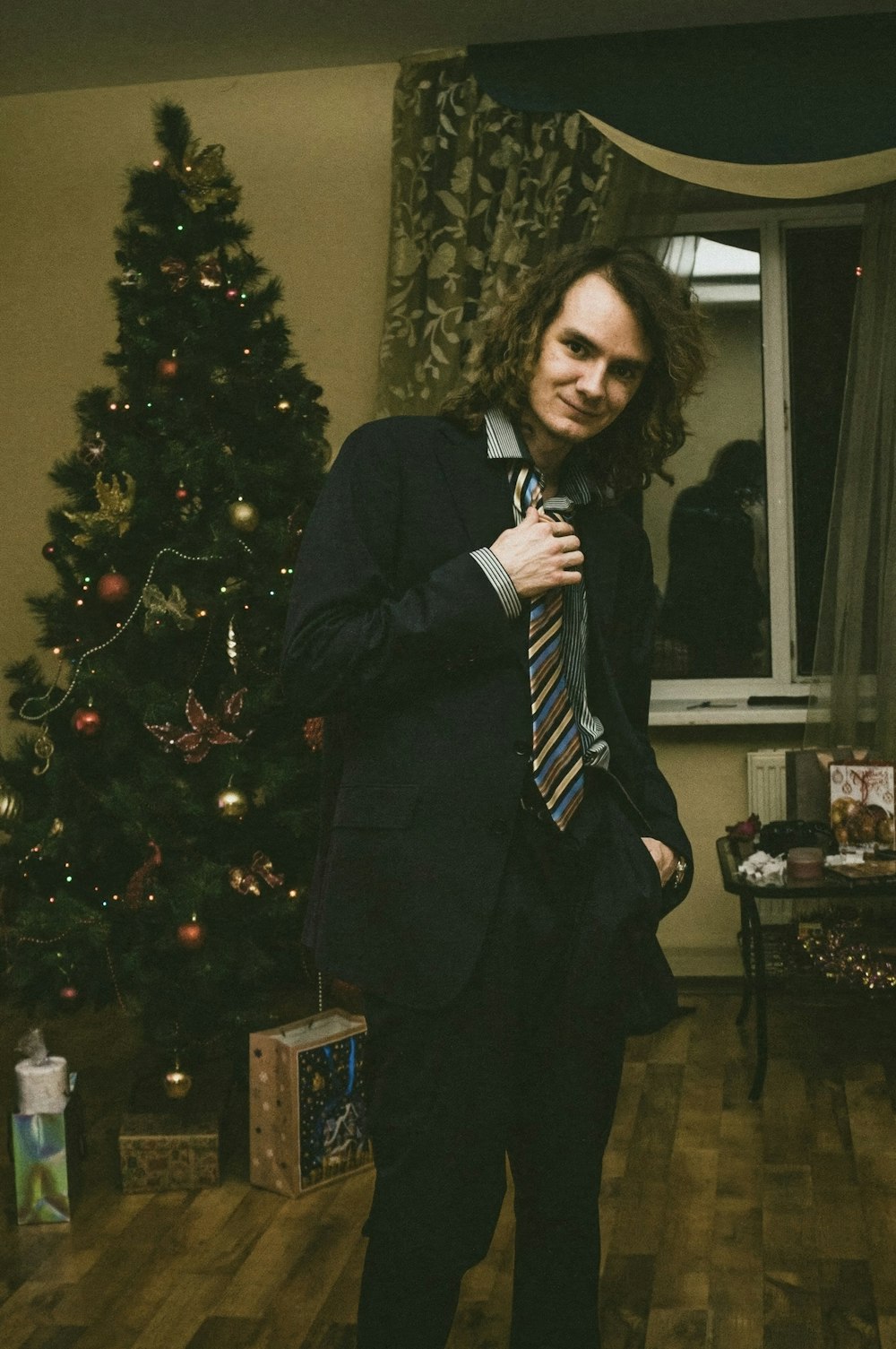 a man in a suit and tie standing in front of a christmas tree