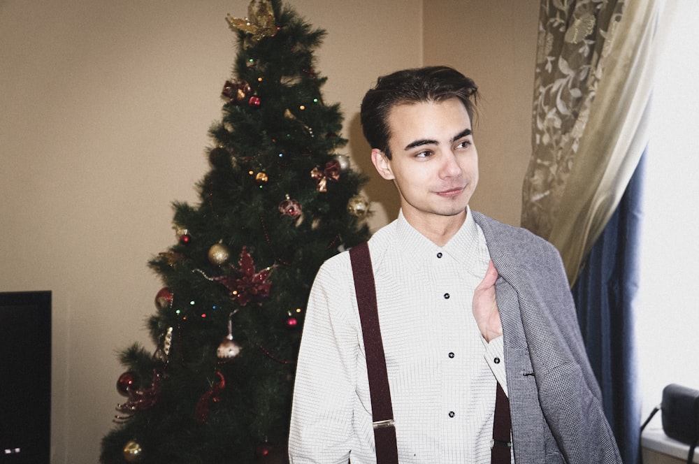 a man wearing suspenders standing in front of a christmas tree