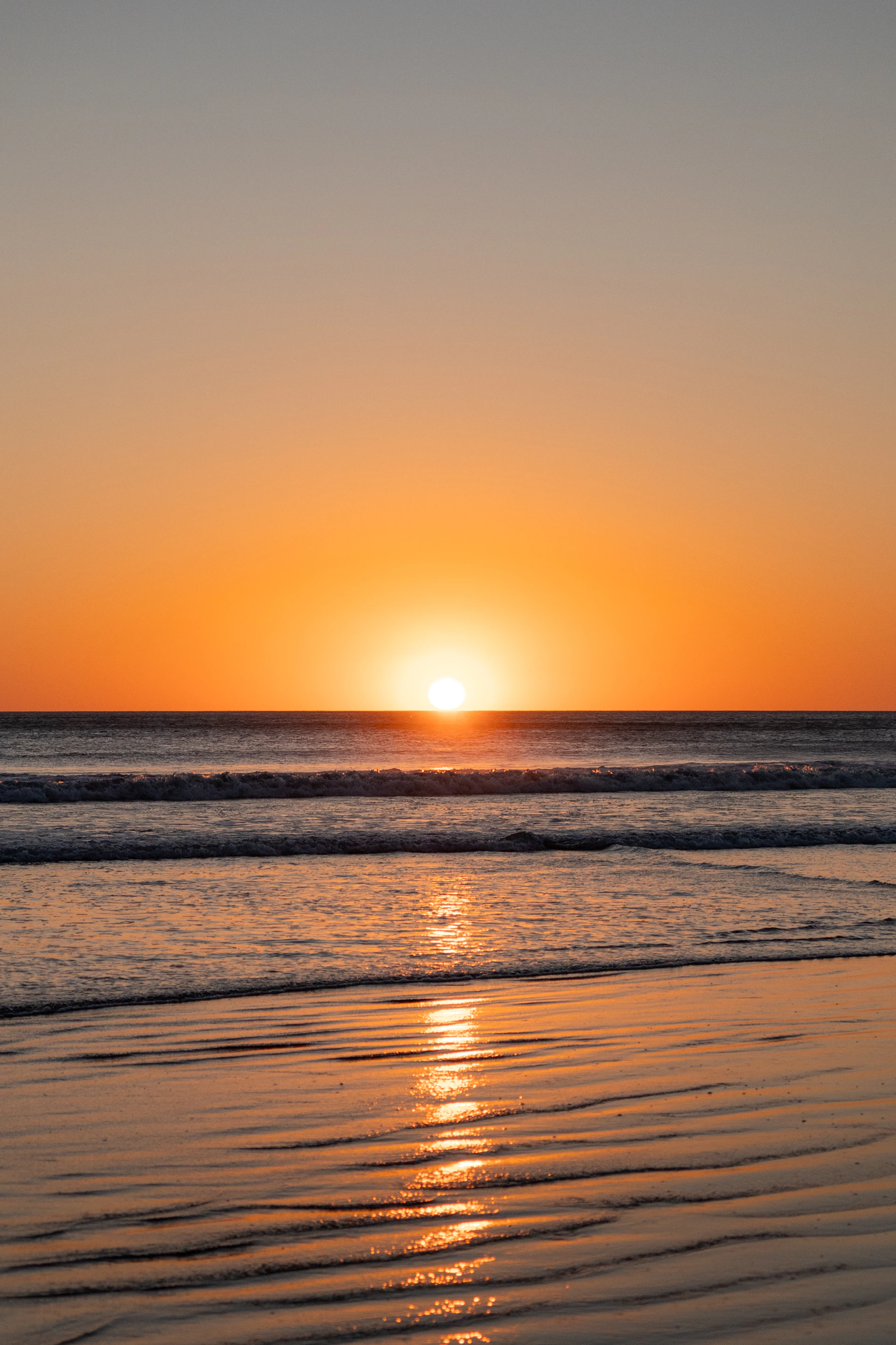 the sun is setting over the ocean on the beach